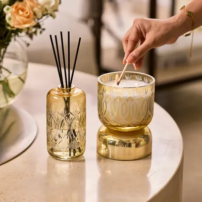 This is my Royal Haze collection. I work with skilled artisans who carry this royal mastery through generations to create the etched art on these ornate cut-glass vessels. Here, I am lighting the candle next to its matching diffuser.