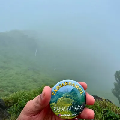 Our Tadiandamol trek badge, held against the misty hills of Coorg. This trek takes you to the highest peak in the Kodagu district.