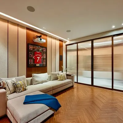 We designed this media room for both cinematic elegance and comfort. The space features a cozy L-shaped sofa, wood and fabric acoustic wall paneling, and a ceiling-mounted projector, with a framed Ronaldo jersey adding a personal touch for our client.