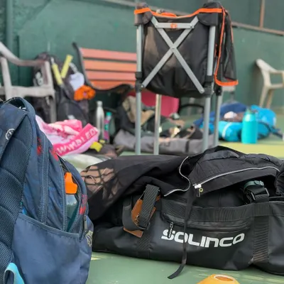 The tools of the trade. A candid shot of tennis bags, water bottles, and equipment on the court, capturing the atmosphere of a busy day of training.