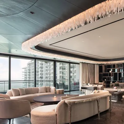 An expansive living area in a DLF Camellias apartment, where curved sofas soften the grand scale of the room. The custom furniture pieces are arranged to create multiple zones for conversation and relaxation, all unified by a neutral palette and luxurious textures.