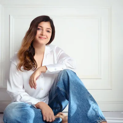 A natural light portrait of a model against a clean white background. The relaxed, seated pose and gentle smile create a warm and approachable headshot, perfect for a portfolio.