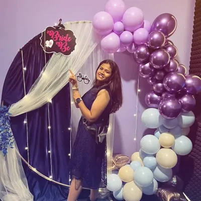 The bride-to-be posing with a 'Bride to Be' sign in front of her custom party decorations. The purple and blue balloon theme was chosen by her friends to surprise her.