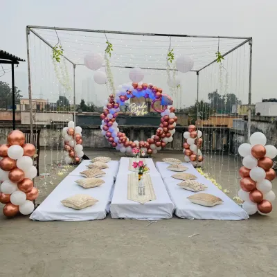 A beautiful 'Bride to be' terrace party setup. This features a metal frame with fairy lights, a circular balloon arch in rose gold and white, and a cozy low-seating arrangement.
