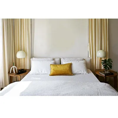 This bedroom is a study in minimalism. The crisp white bedding, neutral walls, and simple wooden side tables create a clean, uncluttered environment. A single pop of color and a monstera leaf add just enough life without overwhelming the senses.