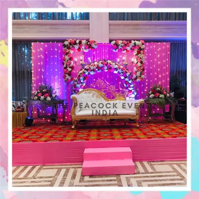 This Roka ceremony stage features a beautiful baby pink backdrop with a floral ring and a classic chandelier for a royal touch. The elevated platform and coordinated colors create a perfect setting for the couple's first official celebration.