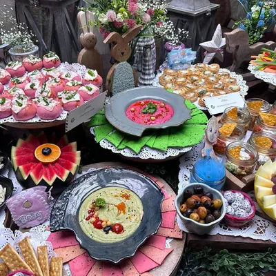 A whimsical baby shower spread with a woodland theme, featuring bunny figurines and floral arrangements. The table is laden with colorful dips, fresh fruits, and bite sized appetizers, creating a magical atmosphere.