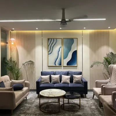 This living room in Noida was designed to be bright and airy. The neutral color palette is accented by the blue sofa and artwork, while the mix of seating encourages social gatherings.
