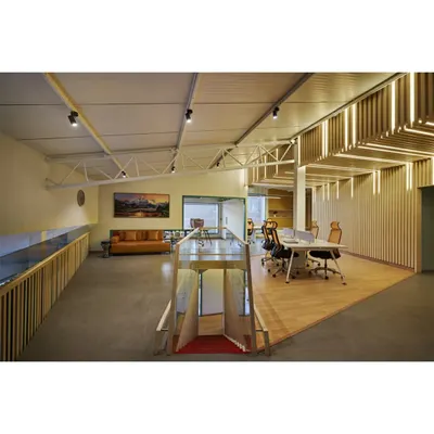The upper level of the Kadence Office, showing the open-plan workspace and lounge area. The design preserves the building's original industrial trusses while introducing a mezzanine and our custom "soundwave" wall, creating a layered and dynamic environment.