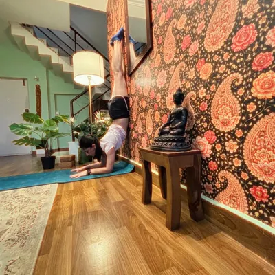 Handstand against a paisley wallpapered wall at home, a small Buddha beside the mat.