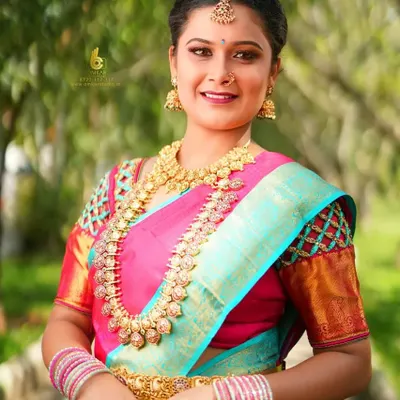 A bright, joyful outdoor portrait showcasing a stunning pink and turquoise silk saree. We use natural light to bring out the rich colors of the fabric and the genuine smile of our client, creating a classic and happy memory.
