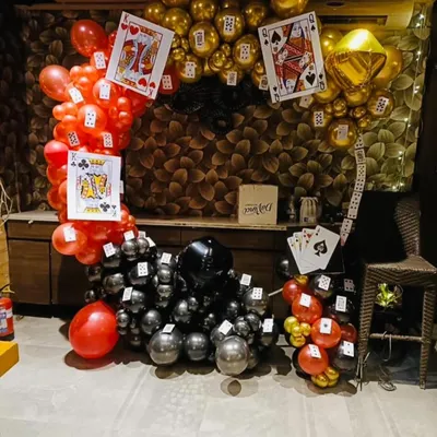 This is a full view of a card party themed balloon decoration. The circular arch is made of red, black, and gold balloons and is decorated with large cutouts of playing cards, creating a perfect backdrop for a casino or card-themed event.