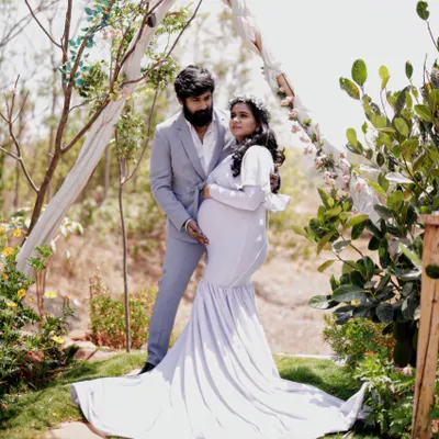 An angelic maternity look for an outdoor shoot. This expecting mother is styled in a white mermaid gown with delicate shoulder bows, creating a soft and serene portrait.