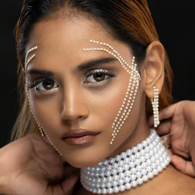 An editorial beauty portrait with a model adorned with pearls on her face and a pearl choker, showcasing a creative and high-fashion makeup look.