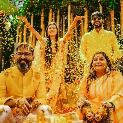 A perfect family moment at the Haldi ceremony. The couple is showered with marigold petals by their loved ones, creating a vibrant and joyous scene filled with laughter and blessings.
