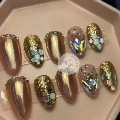 A set of glamorous, party-ready press-on nails. This custom design features gold chrome, chunky glitter, and nails fully encrusted with large, iridescent geometric crystals.