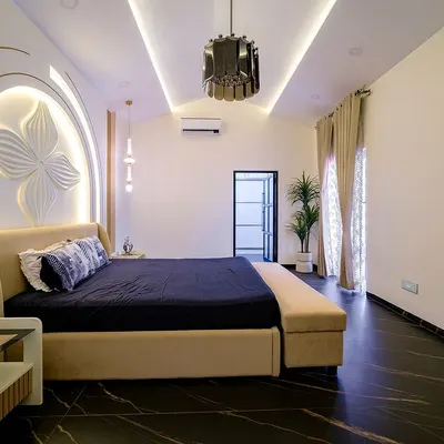 This master bedroom is a study in modern luxury. The dramatic arched headboard features a 3D floral relief, beautifully illuminated to create a soft glow. The dark marble flooring provides a stunning contrast to the light, neutral tones of the bed and walls.