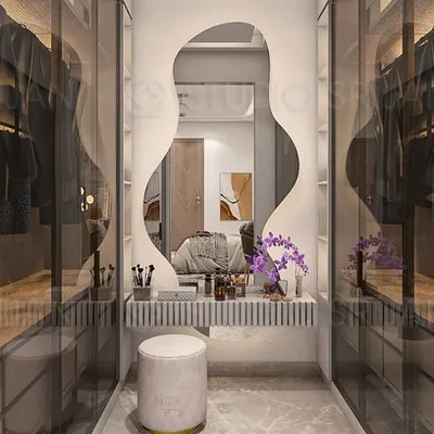 A dedicated dressing and vanity area, featuring a beautifully lit, organically shaped mirror. The walk-in closet is visible through smoked glass doors, creating a sense of depth and luxury.