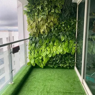 A complete balcony makeover featuring a dense artificial green wall for privacy and a soft artificial lawn, turning a standard balcony into a private garden.
