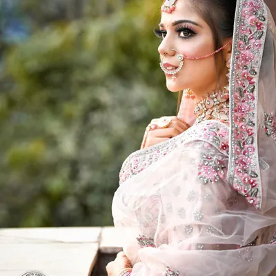 This bridal portrait focuses on the bride's stunning profile and the delicate details of her pastel pink lehenga and dupatta. The soft, diffused daylight enhances her features and creates a dreamy, romantic mood perfect for a wedding album.