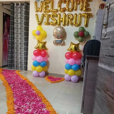 A colorful and happy welcome home decoration for baby Vishrut. The setup includes a path of marigold and rose petals, balloon pillars, and gold foil letters.
