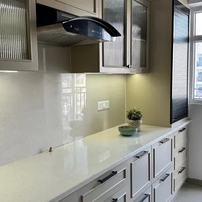 A sleek and modern kitchen at our Nirala Estate project, featuring beige paneled cabinets, black hardware, and fluted glass upper cabinets for a touch of texture.