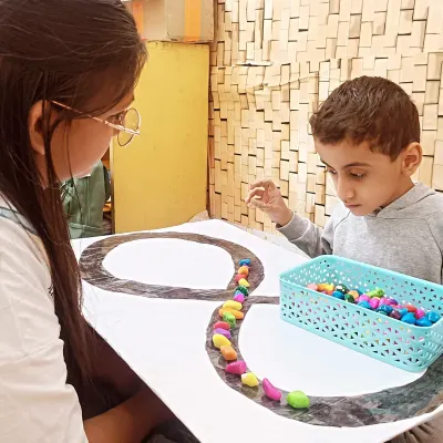 In our ABA therapy sessions, we use tactile activities to improve focus and fine motor skills. Here, a child carefully places colorful stones along a line, an exercise that builds concentration and hand eye coordination.