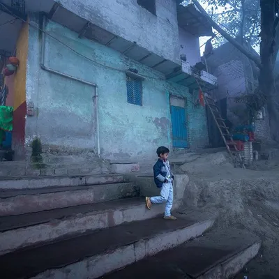 A young boy descends stone steps on a foggy morning at the Yamuna ghat, the mist creating a soft, painterly quality in this environmental shot.