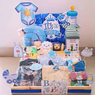 An 'It's a Boy' hamper packed with a variety of clothes, a dancing cactus toy, and other essentials. The blue theme is carried throughout, from the decorations to the baby items.