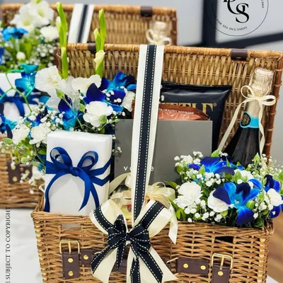 This luxurious picnic basket hamper is the essence of a grand celebration. It features a bottle of fine champagne nestled among fresh blue and white orchids, premium chocolates, and other curated items, all presented in a classic wicker basket with leather straps. It’s a perfect statement gift for milestones like anniversaries, significant birthdays, or corporate achievements.