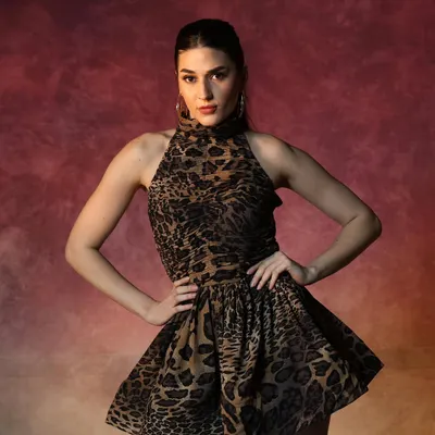 A powerful shot from a fashion campaign. The makeup features a strong, defined brow and contoured cheekbones to create a striking look that complements the bold, animal-print dress and dramatic lighting.