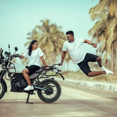 The ultimate shot for adventurous souls. A groom leaps joyfully in mid-air beside his bride on a Royal Enfield, capturing a moment of pure, uninhibited fun.