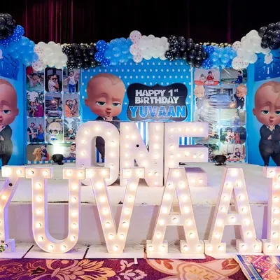 This Boss Baby first birthday stage was a huge hit. I used large marquee letters to spell out the name "YUVAAN" and created a custom backdrop filled with photos from his first year, surrounded by a blue, black, and white balloon garland.