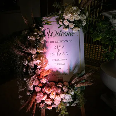 An elegant welcome to Riya and Ishaan's reception. The signage was framed with a lush arrangement of white roses and dried pampas grass, creating a sophisticated and romantic first impression for the evening event.