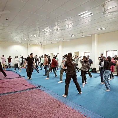 A mixed group of men and women practicing defensive stances in a large indoor session.