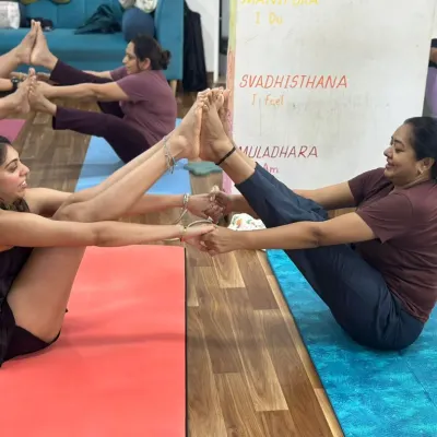 Move, flow, and grow together. Two members of our tribe connect in a partner boat pose, supporting each other to find balance and strength.