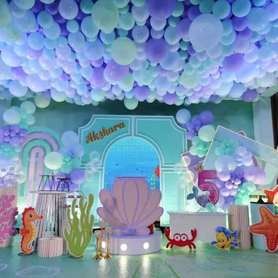 An immersive under-the-sea theme with a ceiling covered in blue and purple balloons to simulate water. The stage features a large shell prop and various sea creature cutouts.