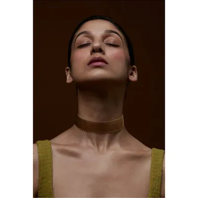 A serene and graceful portrait designed to highlight a statement choker. The model's closed eyes and the warm, earthy tones create a meditative mood, allowing the intricate gold jewellery to be the sole focus.