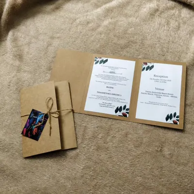 This tri-fold invitation is crafted from sturdy kraft paper, giving it a simple, rustic feel. It's tied with natural twine and features a small, colorful tag with a custom illustration of the couple.