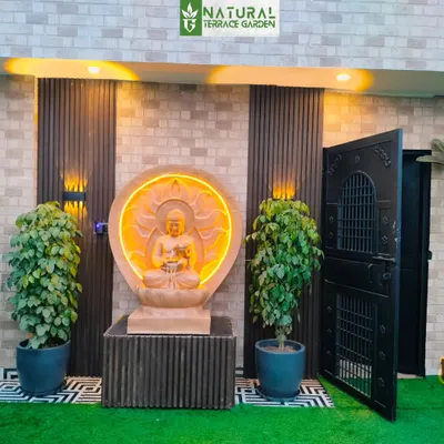 A serene entrance to a terrace garden in Uttam Nagar, featuring a custom-lit sandstone Buddha statue flanked by lush plants.
