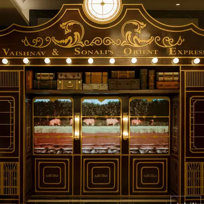 The grand entrance to the Sangeet, designed to look like a vintage train carriage named "Vaishnav & Sonali's Orient Express." The rich wood paneling, gold detailing, and LED screens showing moving landscapes immediately immersed guests in the theme.
