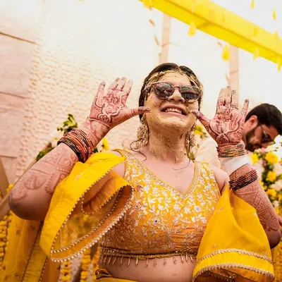 Nothing beats the pure, unscripted fun of a Haldi ceremony. This bride, covered in turmeric paste and sporting sunglasses, shows off her mehndi with a huge smile. We capture these happy, candid moments.