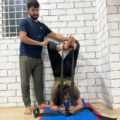Using straps to achieve correct form in Pincha Mayurasana (Feathered Peacock Pose). I am providing support to ensure the student's shoulders and core are engaged correctly, building strength for the full inversion.