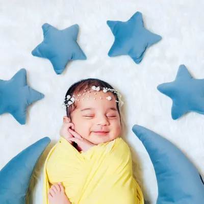 A happy, sleeping newborn swaddled in yellow, nestled on a crescent moon prop. We love capturing these little smiles during our newborn sessions.
