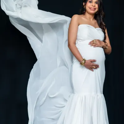 Pure elegance in the studio. This mom-to-be looks stunning in a white strapless gown, with the flowing fabric creating a sense of drama and grace against a simple black background.