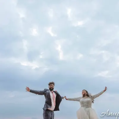 A joyful, carefree moment of a couple with their arms outstretched against a vast, cloudy sky. This shot captures a feeling of freedom and happiness.