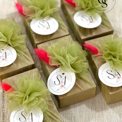 Charming return favors for a special event. These small gifts are wrapped in gold glitter paper and adorned with a fluffy green tulle pom-pom, a pop of pink, and a custom monogrammed tag.