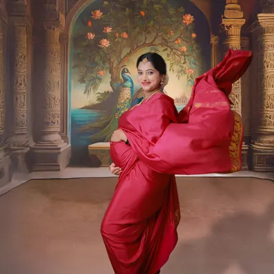 A vibrant and dynamic traditional maternity shoot. The mom-to-be is dressed in a beautiful red saree, with the fabric flowing to create a sense of movement against a painted palace backdrop.