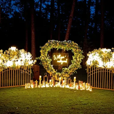 This proposal setup was designed to feel like a secret garden. A large, heart-shaped wreath made of white and green florals frames a neon "Will you marry me?" sign, creating a magical focal point in a serene forest clearing.