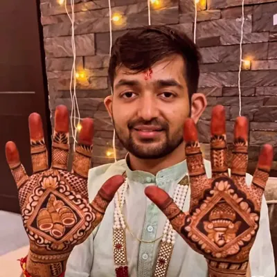 A handsome groom proudly displaying his mehendi, which features traditional symbols like the kalash and Lord Ganesha to bring blessings to his wedding.